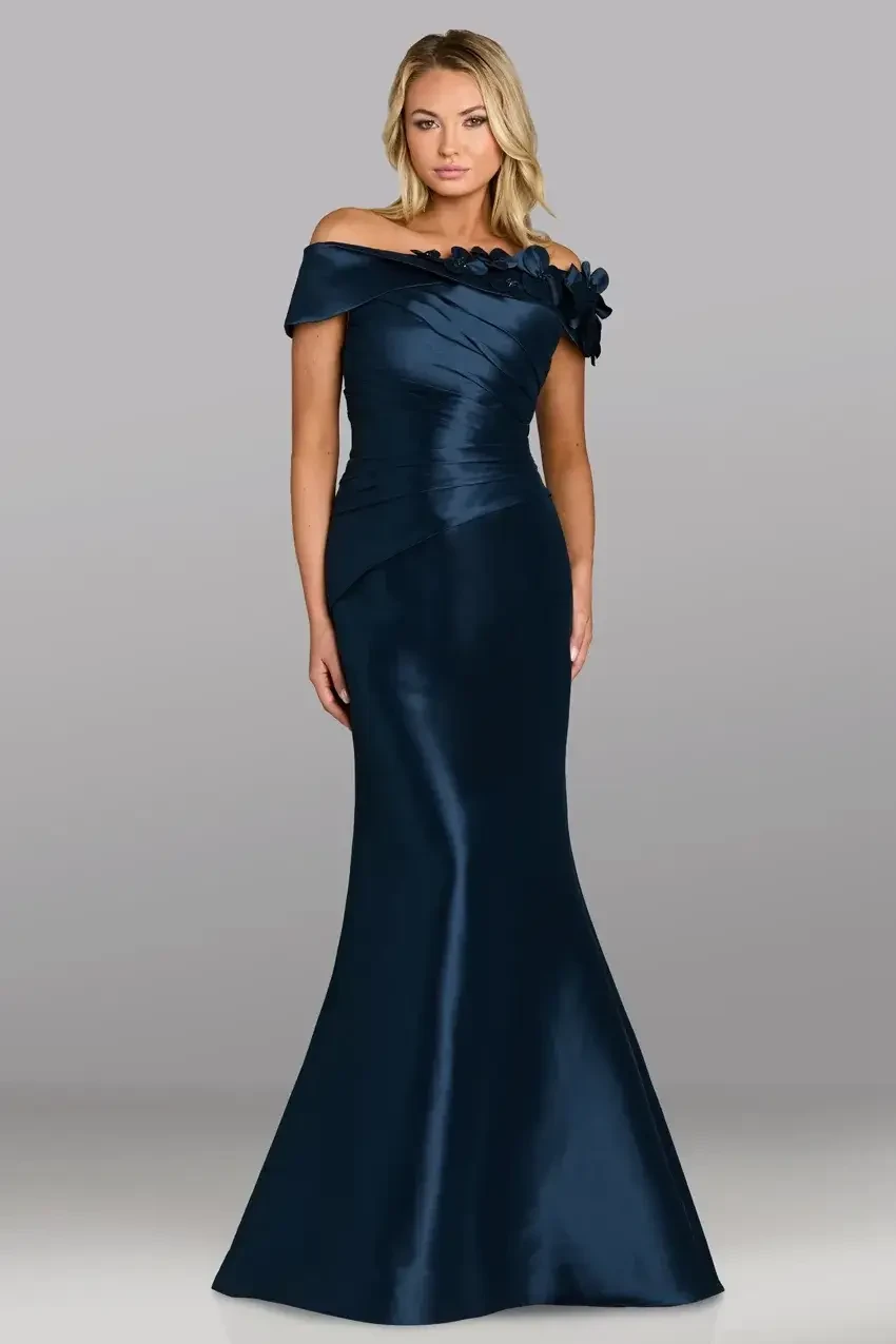 A woman wearing an elegant off-the-shoulder navy blue gown with a fitted silhouette and a flower embellishment on one shoulder.