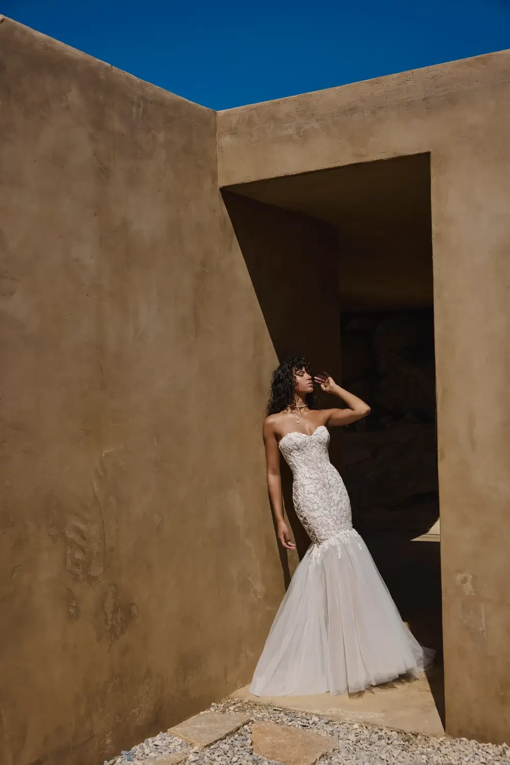A woman in a strapless wedding dress poses near a geometric architectural structure.
